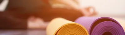 Tapetes de yoga enrolados ao lado de uma pessoa em aula — o tipo de inscrição por horário com limite que o modelo Reserva de Aula do Whocan gerencia